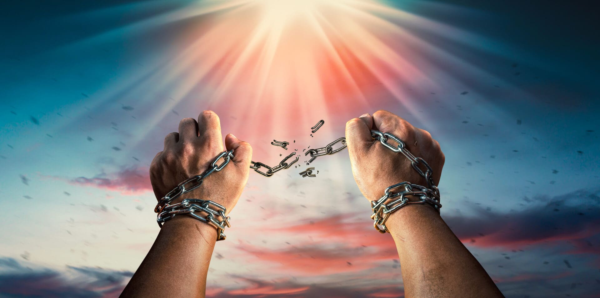 Hands breaking chains under radiant sky.