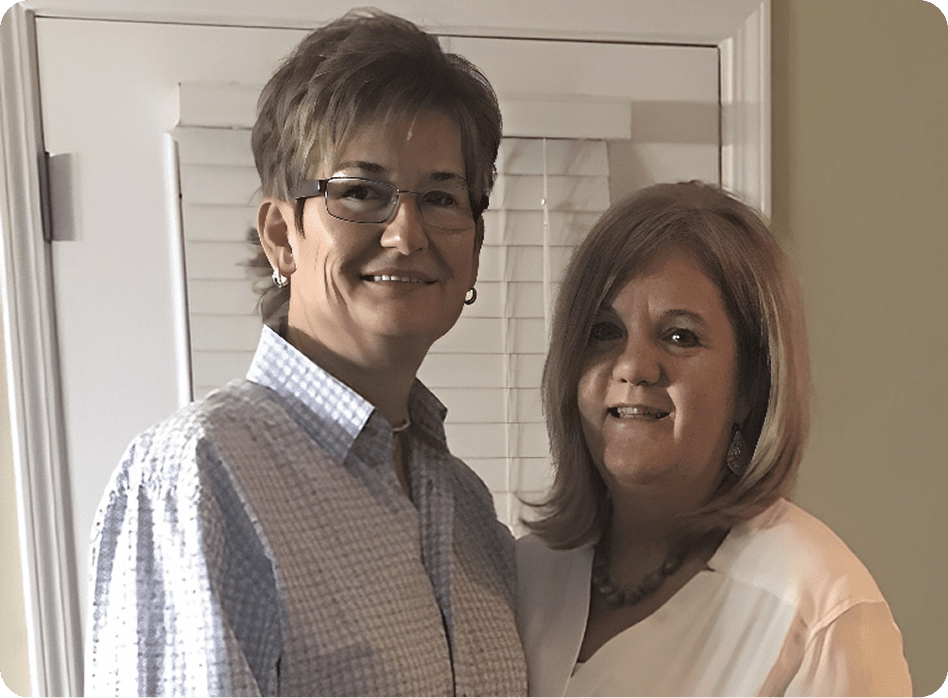 Two people smiling in front of blinds.